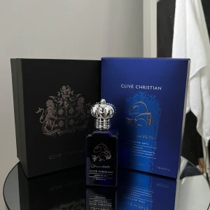 Clive Christian Addictive Arts - Hedonistic 50ml - Elegant parfym från Clive Christian i en djupblå flaska med silverdetaljer och en dekorativ kork. Förpackningen är lyxig med en svart och blå design. Perfekt för den som söker en exklusiv doftupplevelse.
