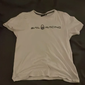 Vit t-shirt från Sail Racing - Säljer en vit t-shirt från Sail Racing med svart logotyp på framsidan. T-shirten har en klassisk rund halsringning och korta ärmar. Perfekt för en avslappnad stil. Pris kan diskuteras 