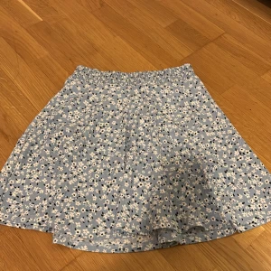 Blommig blå kjol från 157 - Söt blå kjol med blommigt mönster från 157. Kjolen har en elastisk midja för extra komfort och en luftig passform. Perfekt för varma dagar och ger en fräsch look. 🌸