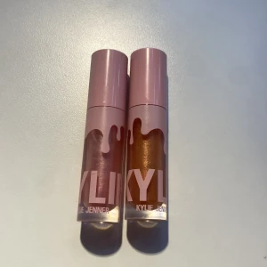 Läppglans från Kylie Jenner - Två läppglans från Kylie Jenner med rosa och guldiga nyanser. Förpackningarna har ett stilrent rosa lock och den ikoniska droppdesignen. Perfekt för att ge läpparna en glansig finish. Säljer eftersom att dem inte kommer till användning.( säljer den för 150kr styck)