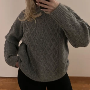 Grå stickad tröja - Mysig grå stickad tröja med ett flätmönster. Tröjan har långa ärmar och ribbade muddar vid ärmslut och nederkant. Från Lager 157 i storlek XS. Aldrig använd. Köparen står för frakten. 🩷