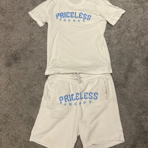 Vit t-shirt och shorts från Priceless Trends - Skick 7/10 / hela dressen säljs ihop | Snyggt set med vit t-shirt och matchande shorts från Priceless Trends. T-shirten har ett tryck i blått framtill och är kortärmad. Shortsen har samma blå tryck och dragsko i midjan för justerbar passform. Perfekt för en avslappnad stil.