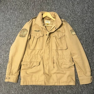 Polo Ralph Lauren Field Jacket - Ovanlig field jacket från Ralph Lauren i färgen desert khaki. Köpt helt ny för 5500:-, går knappt att hitta längre, knappt använd då den är för stor för mig. Inga märkbara defekter. Skriv gärna om ni har frågor eller vill ha bilder på hur den sitter.