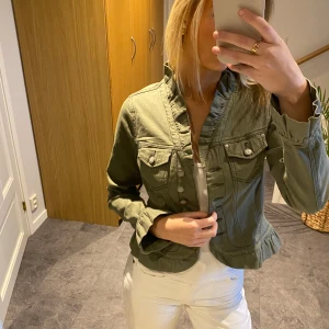 Grön jacka från KappAhl - Säljer en snygg grön jacka från KappAhl med knappar framtill och två bröstfickor. Jackan har en figursydd passform och långa ärmar. Perfekt för en stilren look!