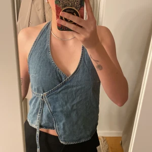 Omlottopp i jeans - Snygg jeansfärgad omlottopp med halterneck-design och öppen rygg. Toppen har en knytning i sidan. 