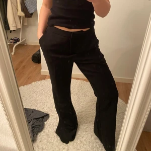 Svarta kostymbyxor - Snygga svarta kostymbyxor med hög midja och bootcut-stil. Perfekta för en stilren look. Byxorna har en dragkedja framtill och är tillverkade i ett bekvämt material. Från Nelly