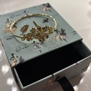 LA FLEUR MULTI CUFF ARMBAND från iokou - Elegant guldarmband med vackra blomdetaljer och en gnistrande sten i mitten. Aldrig använt!Ny pris:599
