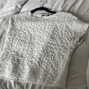 Vit strukturerad topp från Zara - Säljer en vit topp från Zara med unik strukturerad och krinklad yta. Toppen har rund halsringning och korta ärmar. Perfekt för dig som gillar en enkel men ändå intressant look.