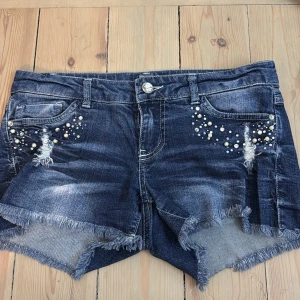 Mörkblå jeansshorts med pärldetaljer - Snygga mörkblå jeansshorts från Only med slitna detaljer och fransig kant. Shortsens fram- och bakfickor är dekorerade med pärlor💘💕