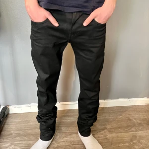 Svarta jeansbyxor från Replay Anbass - Säljer ett par svarta Replay Anbass jeans med klassisk femficksdesign och diskret Replay-logga vid fickan. Jeansen har normal passform och är tillverkade i stretchigt material för extra komfort.