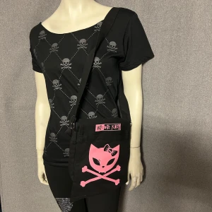 Svart axelväska med rosa kattmotiv - Cool svart axelväska med stort rosa tryck av en katt med korslagda ben och texten 'Bye Love Kitty'. Väskan har justerbar axelrem och är perfekt för dig som gillar alternativ stil.