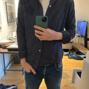 Mörkblå skjorta från Les Deux - Säljer en stilren mörkblå skjorta från Les Deux. Skjortan har klassisk krage, knäppning framtill och långa ärmar. Perfekt för en sommarkväll då materialet är lite tjockare än vanliga skjortor 