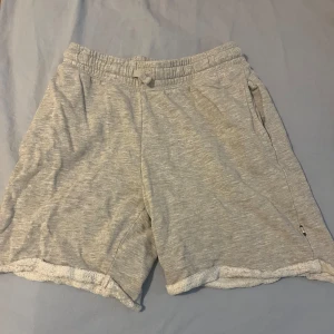 Ljusgrå mjukisshorts med resårmidja - Mysiga ljusgrå shorts i mjukt material med resår och snörning i midjan. Shortsen har fickor på sidorna och en avslappnad passform, perfekta för chill dagar eller träning.