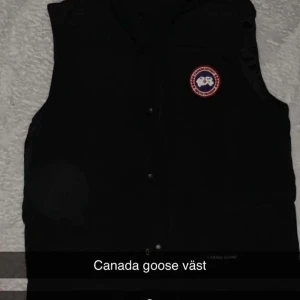 Svart dunväst från Canada Goose - Säljer en svart dunväst från Canada Goose med klassisk logga på bröstet. Västen har knappar framtill och en stilren design som passar till många olika outfits.