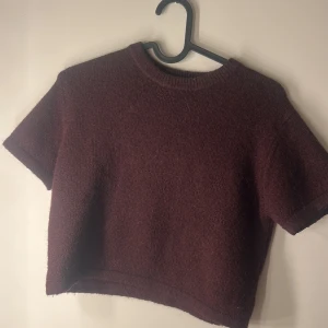  croppad stickad tröja - Säljer en croppad stickad tröja i mörklila färg. Tröjan har korta ärmar och rund halsringning, perfekt för lager-på-lager eller till höstens outfits. Använd en gång.