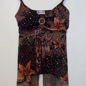 Brun festtopp - Säljer en brun topp med smala axelband, blommigt mönster och glitter från Interco. Den är i mycket bra skick och jag kan inte hitta några skador eller liknande.