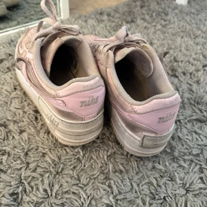 Nike Air Force 1 i rosa  - Säljer ett par Nike Air Force 1 i en snygg kombination av ljusrosa och beige. Skorna har klassisk snörning, perforerad tå och den ikoniska Nike-loggan på sidan. Perfekta för dig som vill ha en stilren och trendig sneaker. (Priset kan diskuteras) 