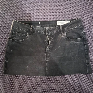Svart jeanskjol från H&M - Svart kort jeanskjol från H&M och har en rak passform och är tillverkad i denim med tydliga sömmar. Perfekt att styla med en enkel topp eller hoodie. Skulle säga att storleken är snäppet mindre än 40/L.