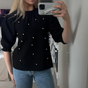 Svart blus med pärlor från Saint Tropez - Säljer en svart blus från Saint Tropez med puffärmar och dekorativa pärlor framtill. Blusen har resår vid halsringning och ärmslut. 