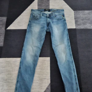 Replay Anbass ljusblå jeans - Säljer ett par Replay Anbass jeans i ljusblå tvätt med klassisk femficksdesign. Jeansen har normal passform och raka ben, med snygga slitningar framtill och bakfickor med diskreta sömmar. Perfekta för en avslappnad stil. Skriv för eventuella frågor och bilder!