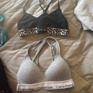 2 Calvin Klein sportiga toppar - Säljer två sportiga toppar från Calvin Klein. En svart med leopardmönstrad kant och en gråmelerad med vit resår och logga. Båda har brottarrygg och elastisk nederkant för extra komfort. 150 kronor för dem båda