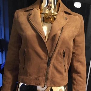Brun mockajacka från H&M Divided - Snygg brun "fusk mocka" jacka från H&M Divided med dragkedja och två fickor framtill. Jackan har en klassisk krage och är perfekt för höst och vår. Den är tillverkad i ett mjukt mockamaterial som ger en stilren look.**Super fint skick **