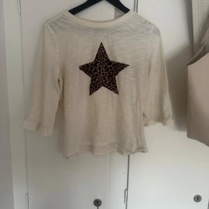 Vit topp med leopardstjärna från GAP - Säljer en vit topp från GAP med en s stjärna i leopardmönster på framsidan. Tröjan har trekvartsärm och är tillverkad i mjuk bomull. Skriv vid intresse eller funderingar🙏