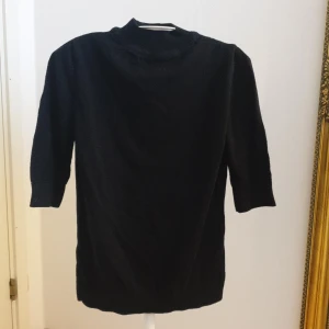 Svart stickad polotröja - En svart stickad polotröja med halvhög krage och trekvartsärm. Tröjan har en enkel och stilren design, perfekt att matcha med olika outfits. Mjuk och bekväm känsla tack vare det stickade materialet. Har tyvärr ingen aning om märke och storlek då lappen är borta men skulle säga att den passar stl S. Superfint skick!