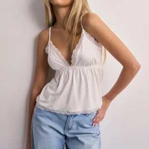 Vit spetsdetaljerad linnetopp - Säljer en söt vit linnetopp med tunna axelband och spetsdetaljer längs v-ringningen och nederkanten. Toppen har en avslappnad passform och är perfekt för varma dagar. Har använd max fem gånger💞