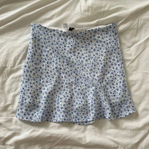 Vit och blå blommig kjol från H&M - Jättegullig kjol från hm! Den har inga tecken på användning och är perfekt till sommaren! Nypris 200kr