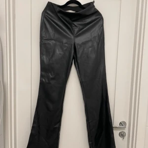 Svarta skinnbyxor från H&M - Säljer ett par svarta skinnbyxor från H&M med bootcut-modell. Byxorna har hög midja ( men går att vika ner) och är tillverkade i syntetmaterial som ger en snygg läderlook. Perfekta för dig som vill ha en trendig och edgy stil.