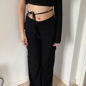 Svarta cargopants med raka ben - Säljer ett par svarta cargopants med raka ben och fickor på sidorna. Byxorna har normal passform och stängs med knapp och dragkedja. Perfekta för en trendig och avslappnad stil.