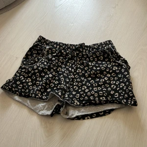Svarta shorts med leopardmönster och knyt - Säljer ett par svarta shorts med beige leopardmönster och elastisk midja med knytband. Shortsen har fickor på sidorna och är tillverkade i mjukt bomullstyg. Perfekta för sommardagar när du vill vara både bekväm och snygg.