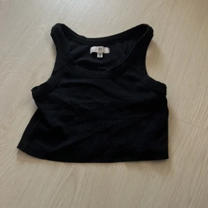 Svart ribbad linnetopp - Säljer en svart ribbad linnetopp från RR. Toppen är croppad och har breda axelband och rund halsringning. Perfekt för sommardagar eller som lager under skjorta eller jacka.