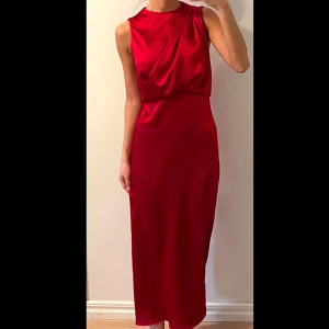 Röd satinklänning  - Säljer en elegant röd långklänning i satin med ärmlös design och snygg drapering framtill. Klänningen har en figurnära passform och rund halsringning. Perfekt för speciella tillfällen (fest, bröllop, högtider) när du vill sticka ut.❤️