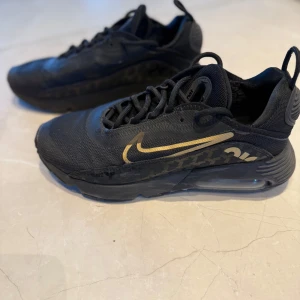 Nike Air Max  - Säljer ett par svarta Nike Air Max 2090 sneakers med guldiga detaljer och mönstrad sula. Skorna har synlig Air Max-dämpning i sulan, snörning och en sportig design. Perfekta för dig som gillar streetwear och vill ha något unikt.