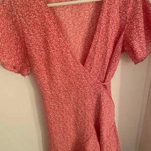 Rosa omlottklänning - Supersöt rosa omlottklänning med vitt blommigt mönster och korta puffärmar. Skitsnygg perfekt nu inför sommaren!🩷