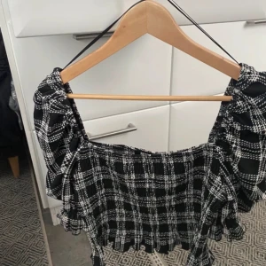 Svartvit rutig croppad topp från BikBok - Trendig croppad topp från BikBok i svartvitt rutigt mönster. Toppen har puffiga långa ärmar och smockad resår vid midjan och ärmsluten. Perfekt för att skapa en cool och stilren look.