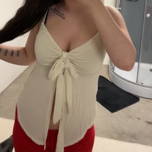 Beige knytlinne med v-ringning från Gina Tricot  - Säljer ett beige linne med v-ringning och knyt framtill. Toppen är ärmlös och har en lös passform, perfekt för varma dagar. Materialet känns lätt och luftigt. Har endast testats!