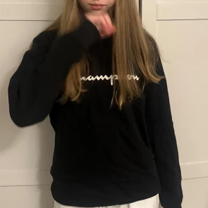 Svart långärmad tröja från Champion - Säljer en svart långärmad tröja från Champion med vit logga tryckt på bröstet. Tröjan har en klassisk passform och är tillverkad i mjuk bomull, perfekt för en avslappnad stil.