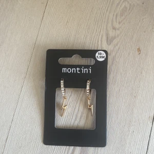 Guldiga blixtörhängen från Montini - Snygga örhängen från Montini med guldiga blixtar som hänger från små hoops dekorerade med glittrande stenar. Perfekta för att ge din look lite edge och extra bling. Kommer på originalkortet från Ur & Penn.