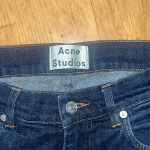 Mörkblå jeans från Acne Studios - Snygga mörkblå jeans från Acne Studios med klassisk femficksdesign och raka ben. Jeansen har orange kontrastsömmar och silverfärgade nitar. Perfekta för dig som gillar stilrena och tidlösa jeans i hög kvalitet. Modellen är ace rinsed och storlek är w31 l32 pytteliten defekt på höger ben, se bild 4