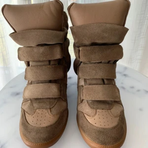 Beige wedge sneakers med kardborre - Chunky sneakers i beige mocka och skinn med högt skaft och flera breda kardborreband. Snygg plattformssula i gummi och vadderad plös för extra attityd. Perfekta för dig som gillar streetstyle och vill sticka ut.