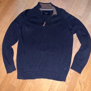Mörkblå halfzip - Snygg mörkblå stickad tröja från Bondelid med half zip och ribbad krage i kontrastfärg. Perfekt för kyliga dagar, med långärmad passform och diskret broderad logga på bröstet. Klassisk och stilren design som funkar till jeans eller chinos.