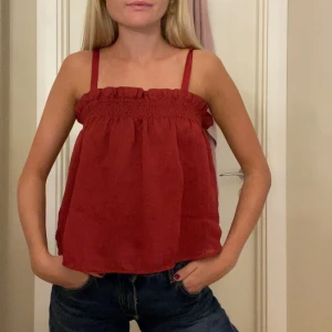 Vinröd linnetopp med smock - Säljer en vinröd linnetopp med smala axelband och smockad överdel. Toppen har en luftig och flowy passform med volangkant upptill. 