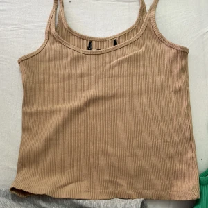 Beige ribbad linnetopp - Säljer en beige ribbad linnetopp med smala axelband. Toppen har en enkel och stilren design, perfekt att matcha med jeans eller kjol. Mjuk och stretchig för en bekväm passform.