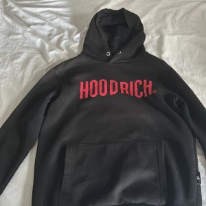 Svart hoodie från Hoodrich med röd logga - Svart hoodie från Hoodrich i storlek small med stor röd HOODRICH-logga på bröstet. Tröjan har huva med snörning och en stor magficka framtill. Mjuk insida och klassisk streetwear-look, perfekt för chill dagar. Passar dig som gillar bold prints och urban stil. Lite solbränd på luvan väldigt lite annars inget fel. Pris kan diskuteras 