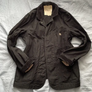 Svart overshirt från Denim & Supply Ralph Lauren - Svart overshirt från Denim & Supply Ralph Lauren med boxig passform. Jackan har breda manchester-detaljer på krage och ärmslut, flera fickor och knäppning framtill. Helt i bomull. Tyget är ganska grovt och av hög kvalitet.