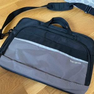Grå och svart datorväska från Targus - Snygg datorväska från Targus i grått och svart med praktiskt axelband och handtag. Väskan har flera fack med dragkedja.