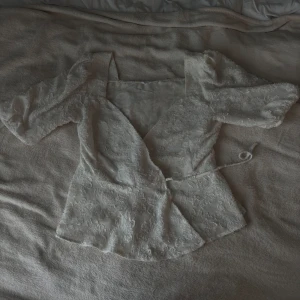 Vit omlottblus med blommor från MNG - Superfin vit omlottblus från MNG med fyrkantig ringning och puffiga halvlånga ärmar. Blusen har ett vackert strukturerat tyg med broderade blommor och knytband i midjan.